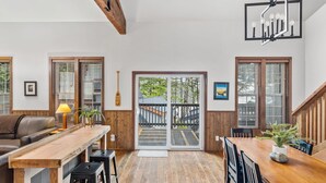 A spacious living area with a wooden dining table, a sofa, and a staircase leading to an outdoor deck. - Private HOT TUB ~ Nature & Beach at Your Doorstep ⎮ Tidal Pool (Ucluelet)