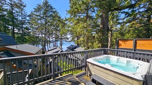 A deck with a hot tub, wooden deck, and a view of a forest and water. - Private HOT TUB ~ Nature & Beach at Your Doorstep ⎮ Tidal Pool (Ucluelet)