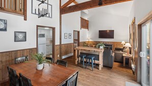 A spacious living area with a wooden dining table, bar, and seating area. A kitchen with modern appliances is visible in the background. - Private HOT TUB ~ Nature & Beach at Your Doorstep ⎮ Tidal Pool (Ucluelet)