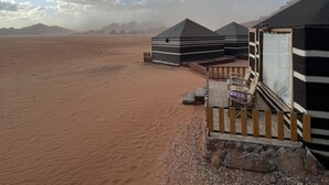 Paisagem desértica com tendas e um deck de madeira com cadeiras.