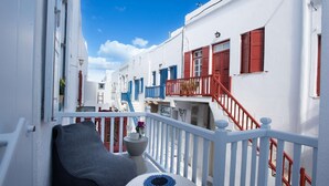 Une rue étroite bordée de bâtiments blancs, de volets rouges et de balcons.