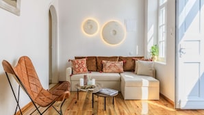 Une pièce dotée d’un plancher en bois, d’un canapé agrémenté de coussins à motifs, d’un fauteuil en cuir et d’un luminaire suspendu.
