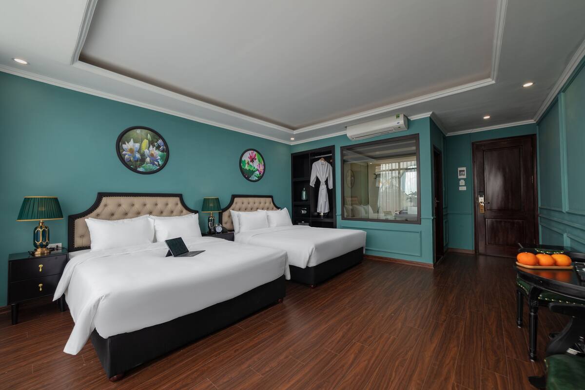 Een hotelkamer met twee bedden, een nachtkastje met een lamp, een dressoir en een tafel met sinaasappels.