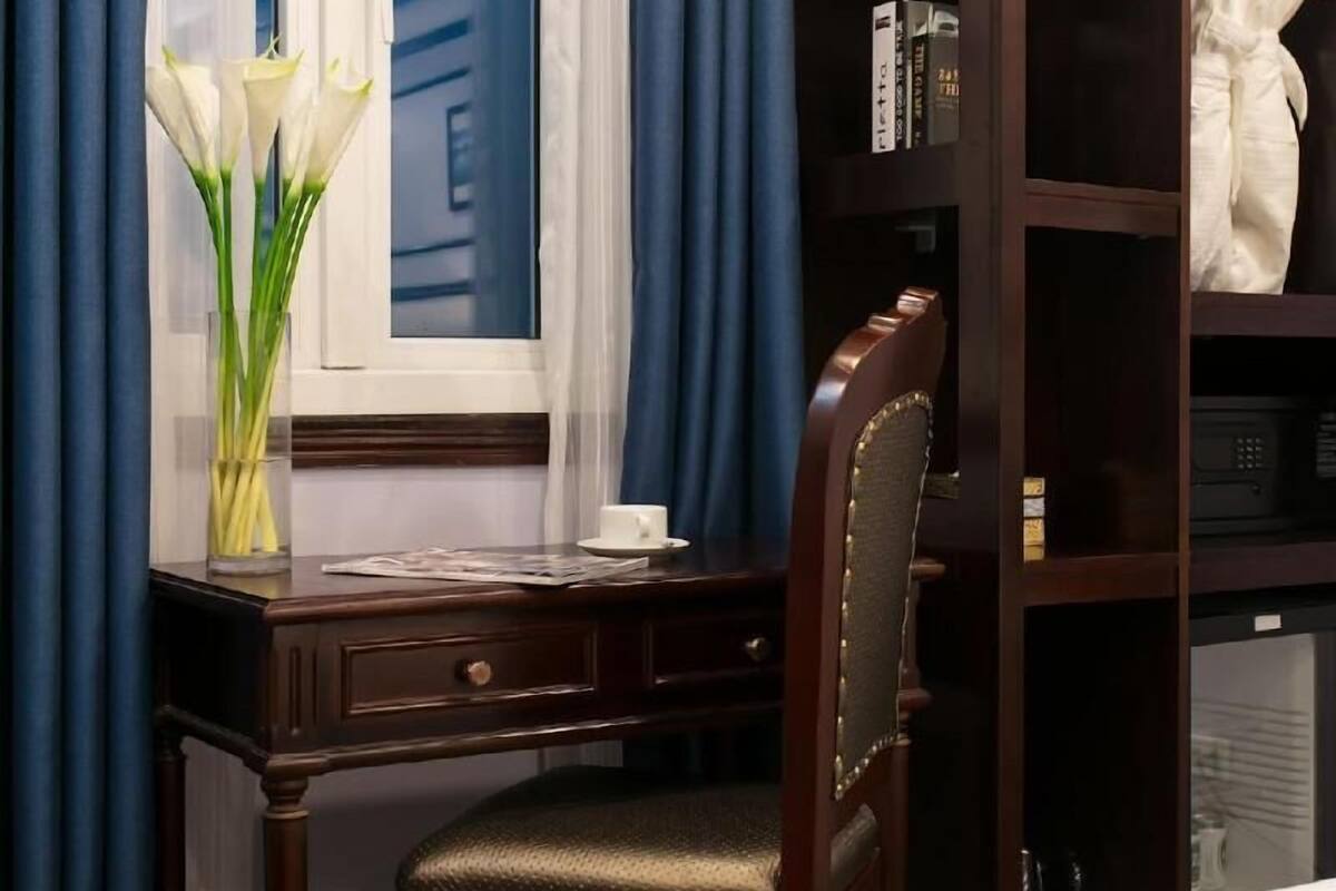 Een hotelkamer met een houten bureau, een stoel, een boekenkast en een bed.