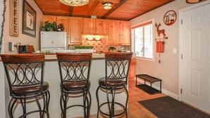 Une cuisine avec des meubles de rangement en bois, un réfrigérateur et un coin bar avec des tabourets.