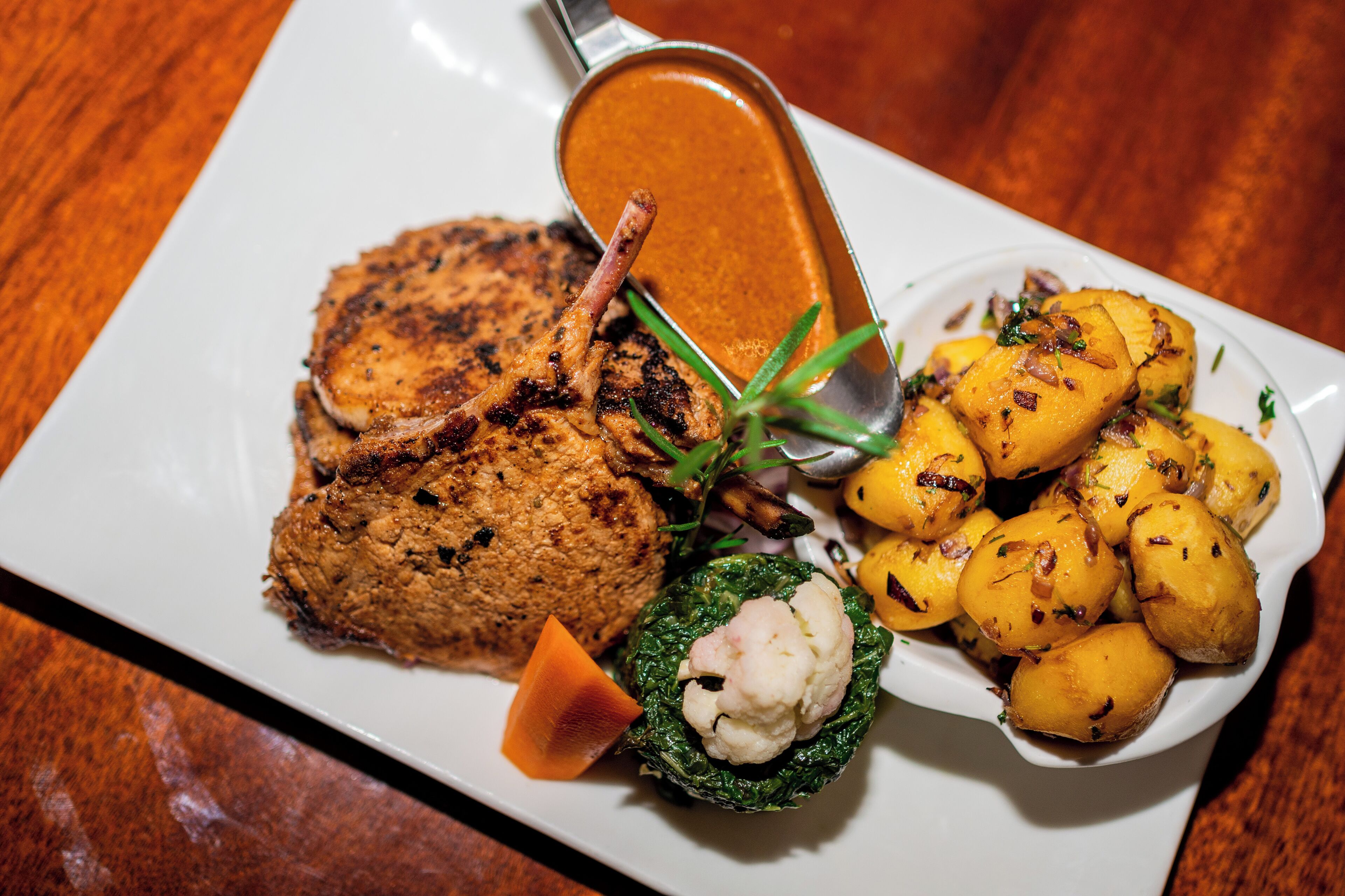 Une assiette composée de viande grillée, de pommes de terre rôties et d’une sauce crémeuse.