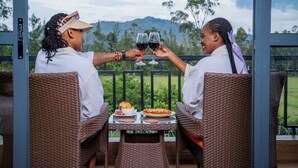 Two people toasting with wine glasses at a table with a scenic view of mountains and trees. - Ciala Resort Best Hotel in Kisumu Kenya (Kisumu)