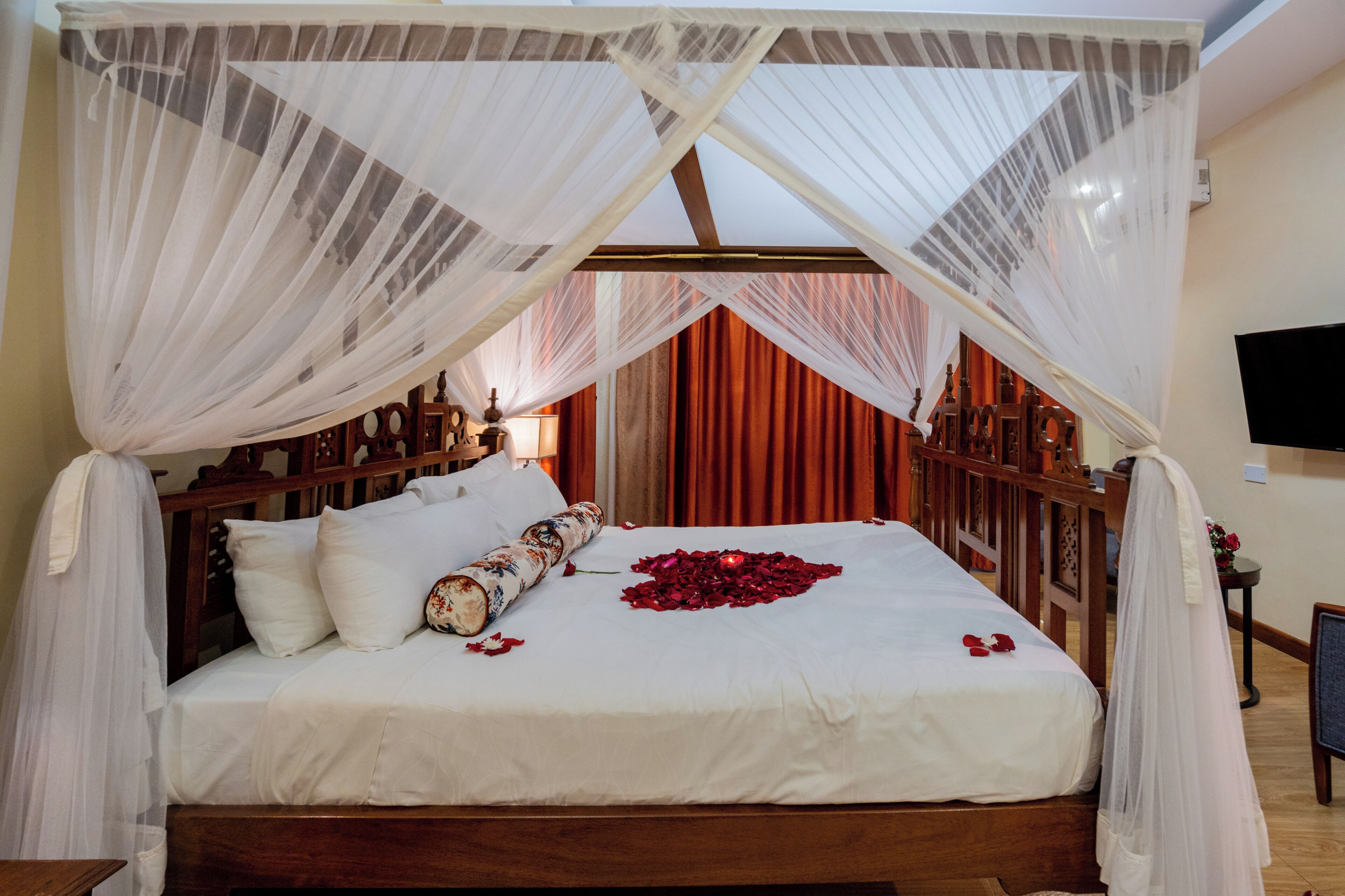 Un letto a baldacchino, con biancheria bianca e petali di rosa rossa.