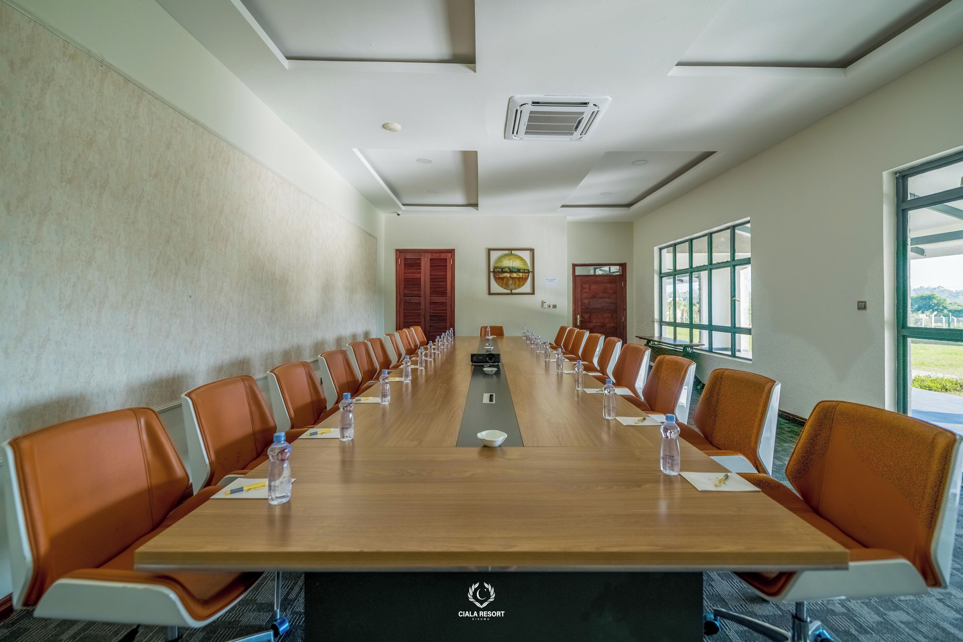 A conference room with a long table, orange chairs, water bottles, and a projector.