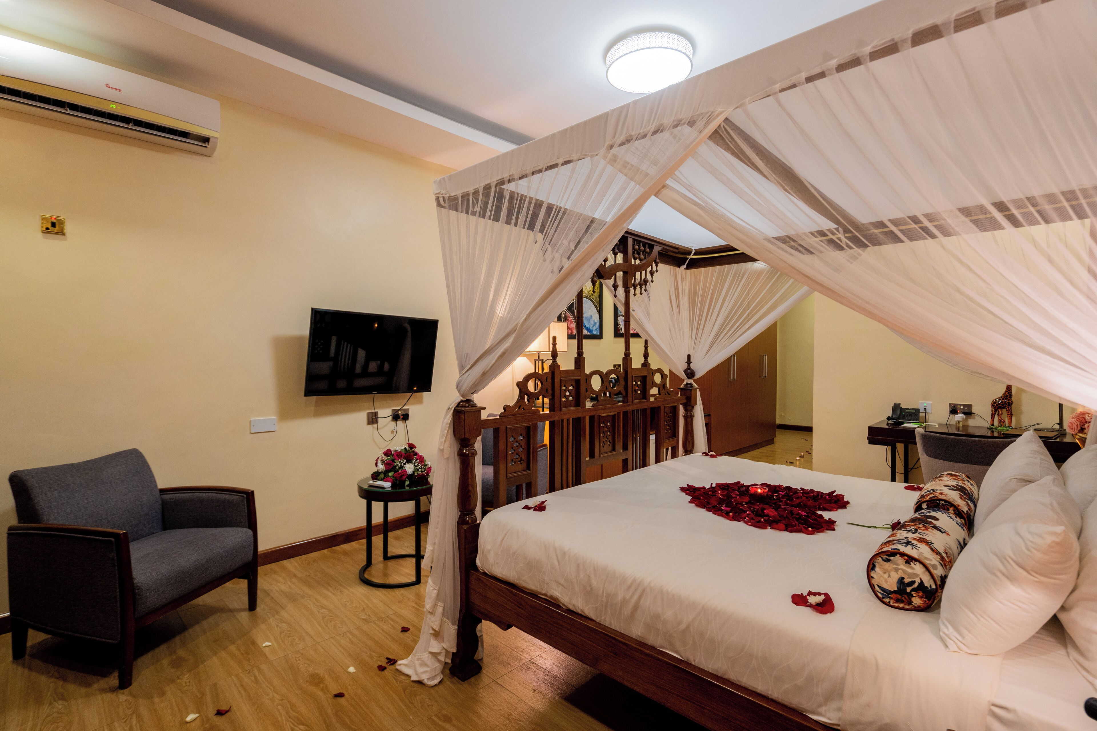 Un dormitorio con cama con dosel, televisor, una silla y una mesita con flores.