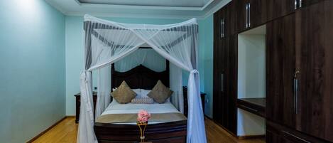 Un dormitorio con cama de dosel, suelo de madera, una mesita de noche con un florero y armarios de madera oscura.