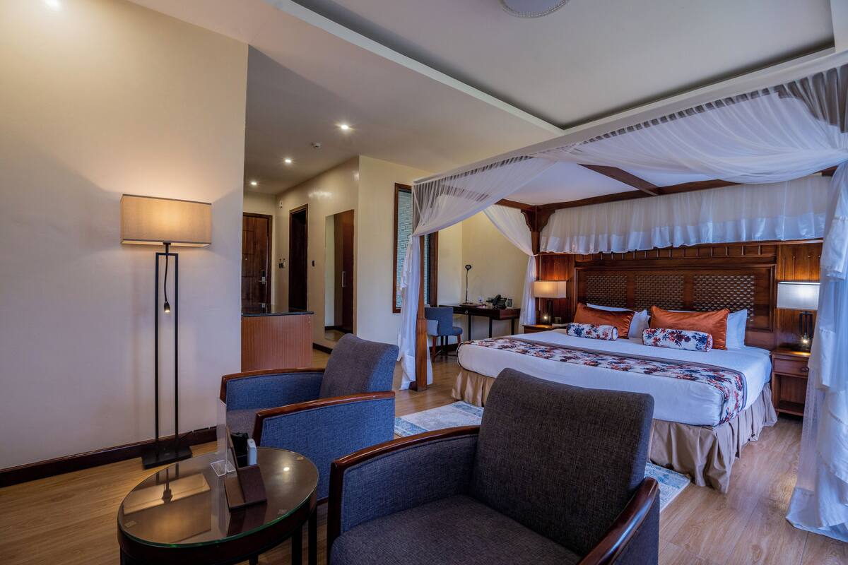 Ein Hotelzimmer mit einem großen Bett, einer Sitzecke mit Sesseln, einem Schreibtisch und einer Lampe.