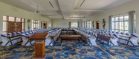 A large conference room with rows of tables and chairs, a podium, and large windows.