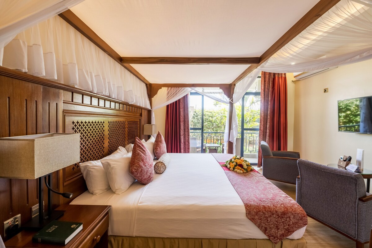 Ein Hotelzimmer mit einem großen Bett, einem Schreibtisch, einem Sessel, einem Fernseher und einem Fenster mit Vorhängen.
