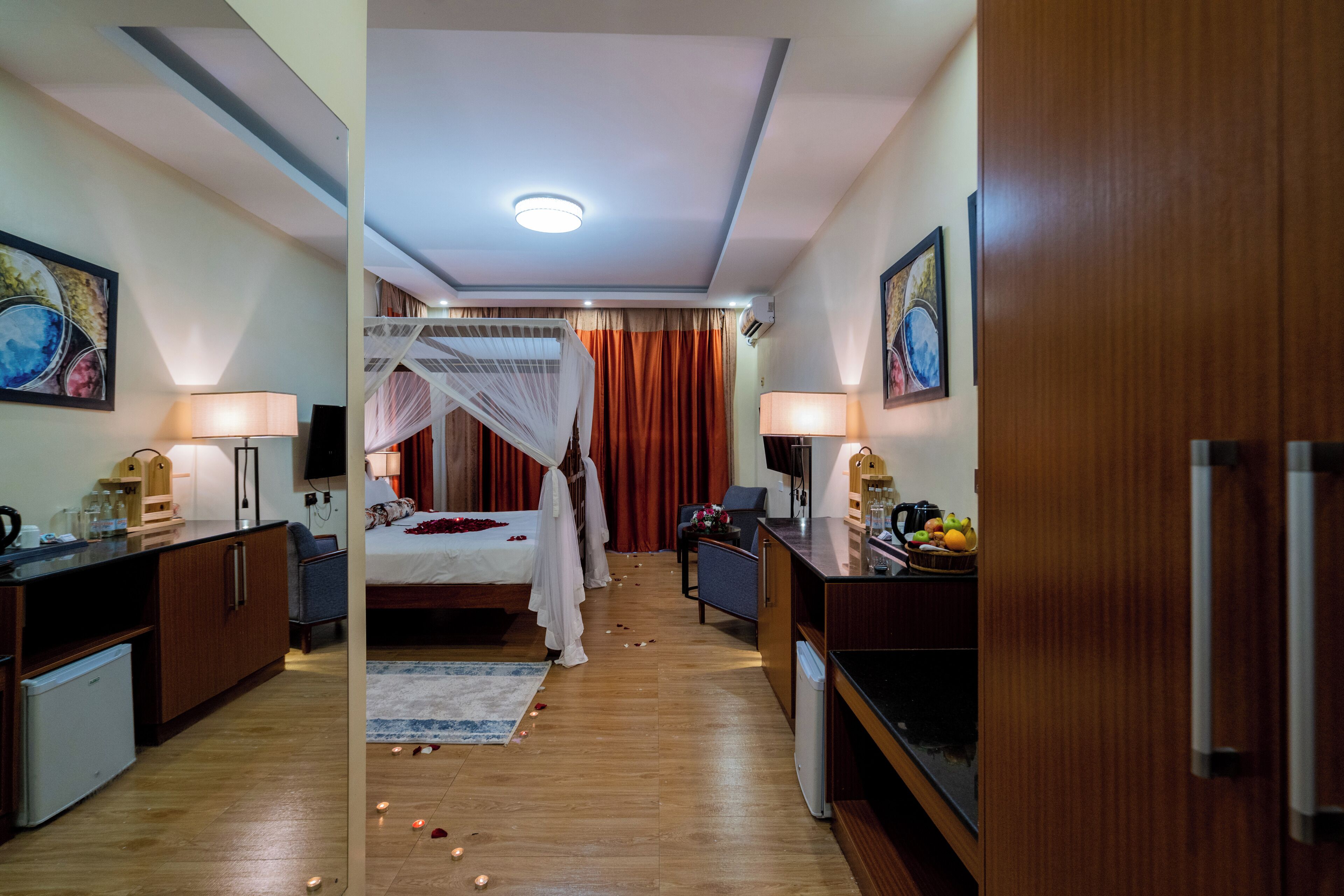 Habitació d'hotel amb llit, taula de nit, làmpada i una cuineta petita.
