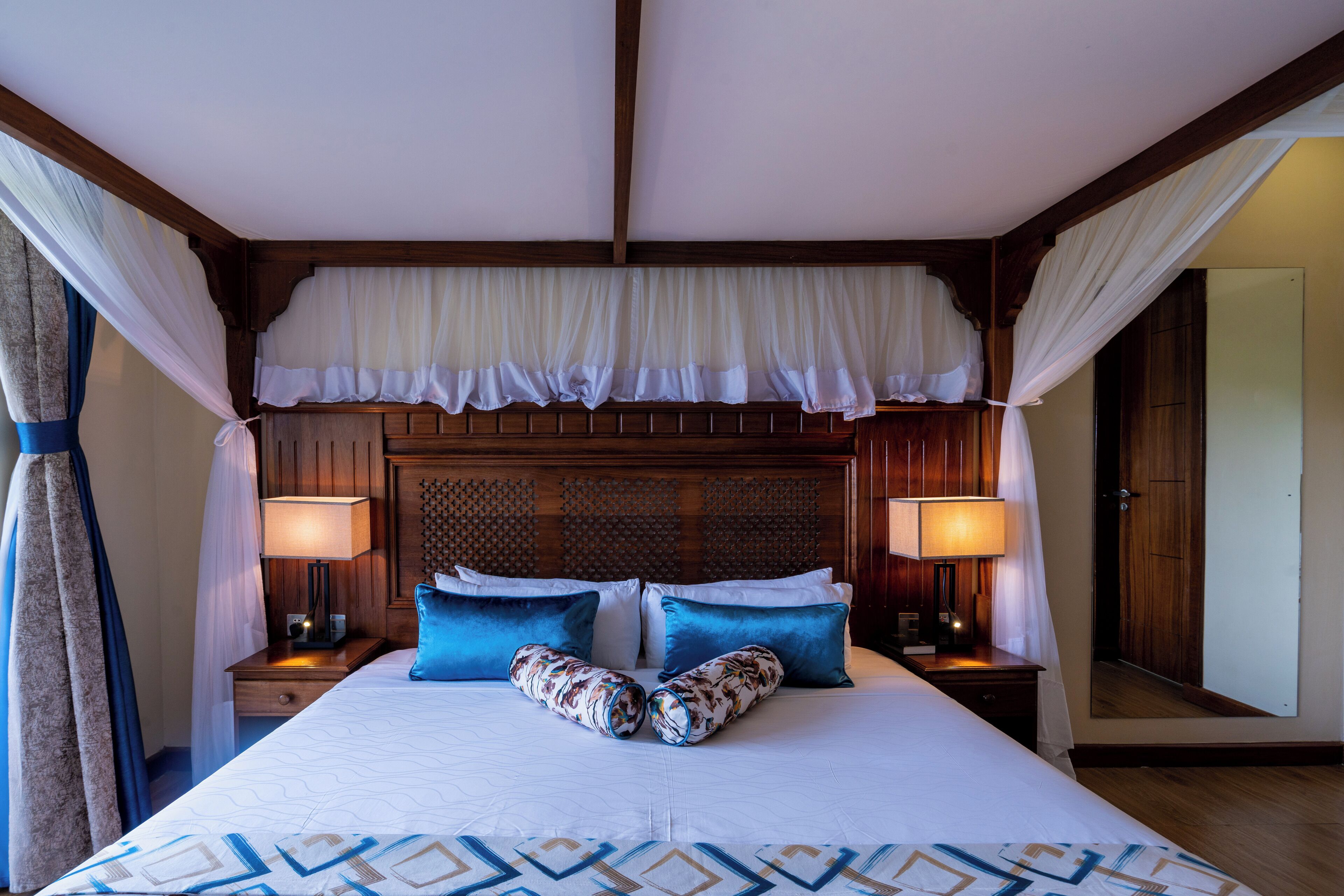 A large bed with a canopy, two bedside tables with lamps, and a wooden headboard.