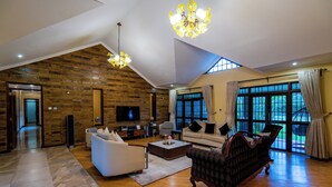A spacious living room with a high ceiling, a fireplace, a television, and large windows with curtains. - Ciala Resort Best Hotel in Kisumu Kenya (Kisumu)