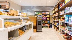 A clean, well-organized grocery store with shelves stocked with various products, a refrigerated display, and a coffee machine.
