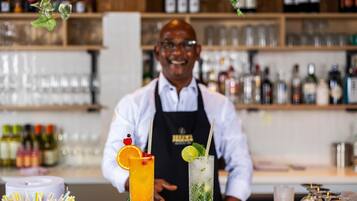 Een bar met een bartender, twee cocktails en diverse flessen op de achtergrond.
