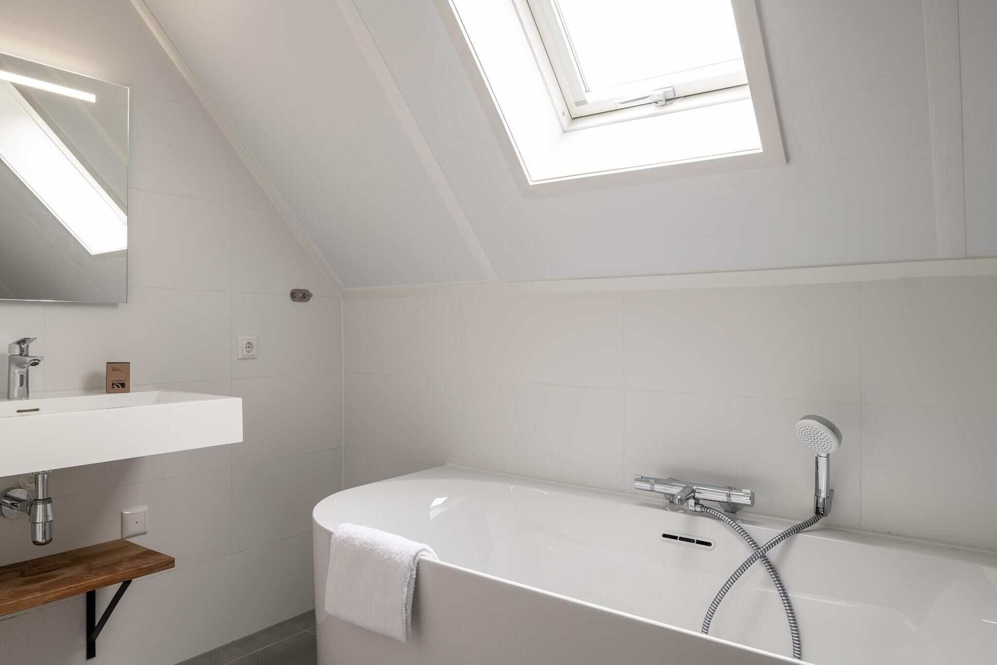 Une salle de bain moderne avec une lucarne, une baignoire blanche, un lavabo et une étagère en bois.