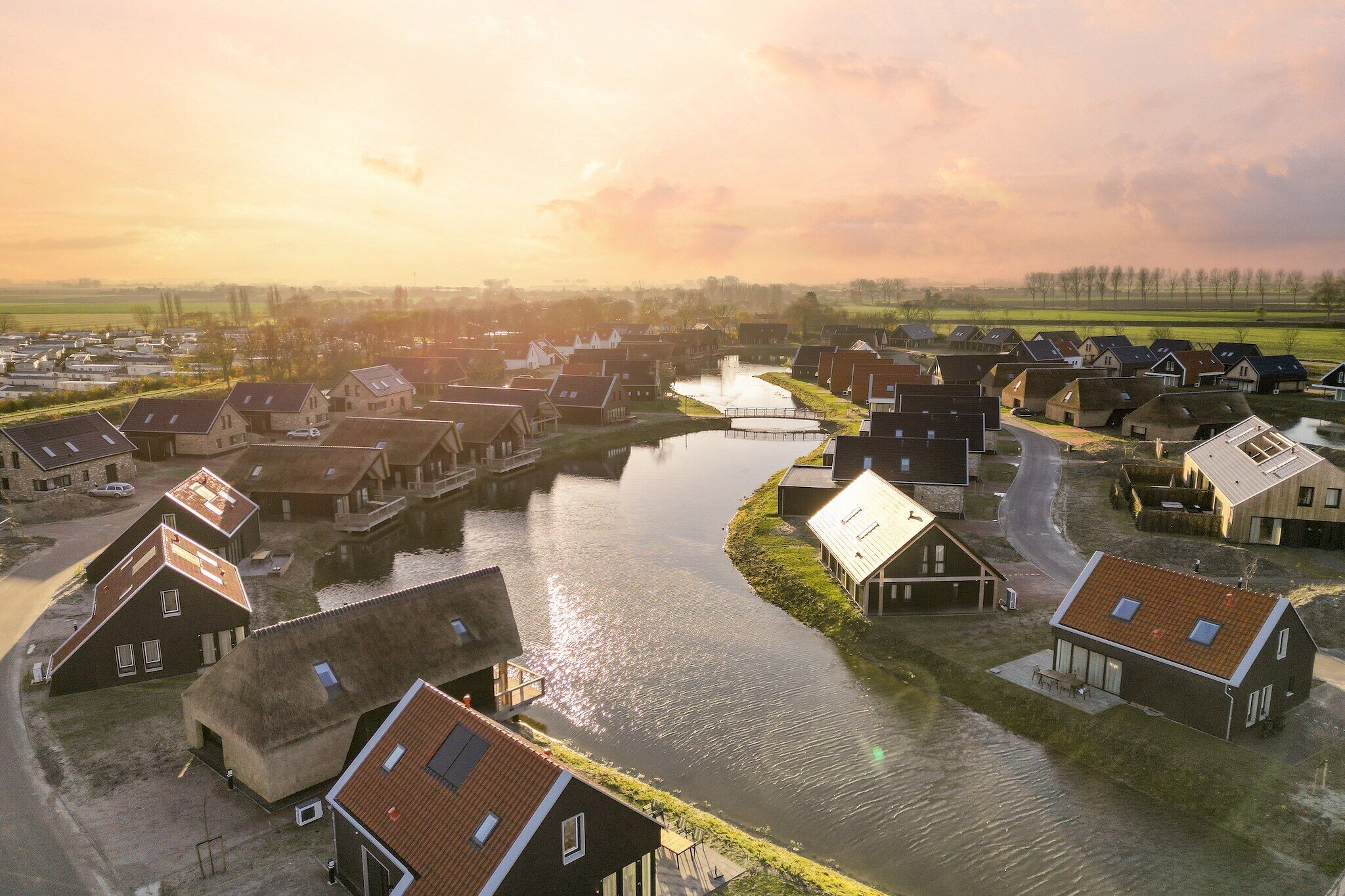 A riverside village with traditional houses, a canal, and a sunset.