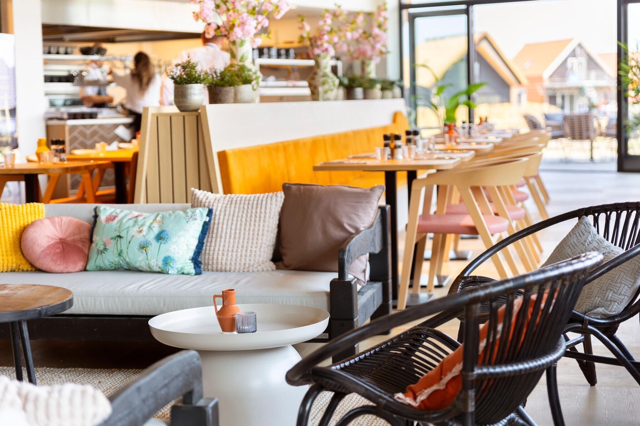 Una cafetería moderna con un área de estar acogedora, que incluye un sofá, sillas y una pequeña mesa con una tetera.