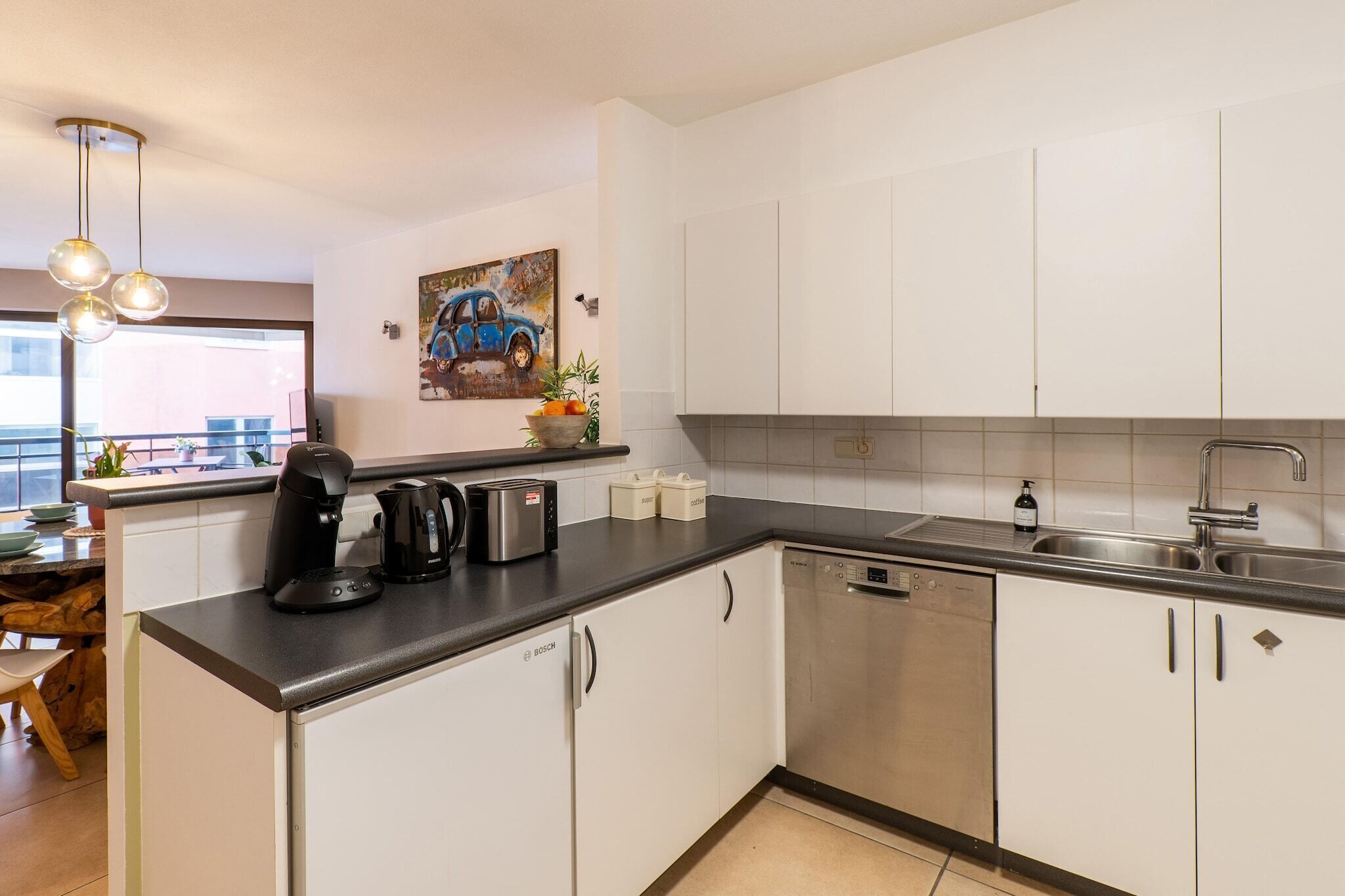 Een moderne keuken met witte kasten, een Bosch vaatwasser, een koffiezetapparaat en een spoelbak.