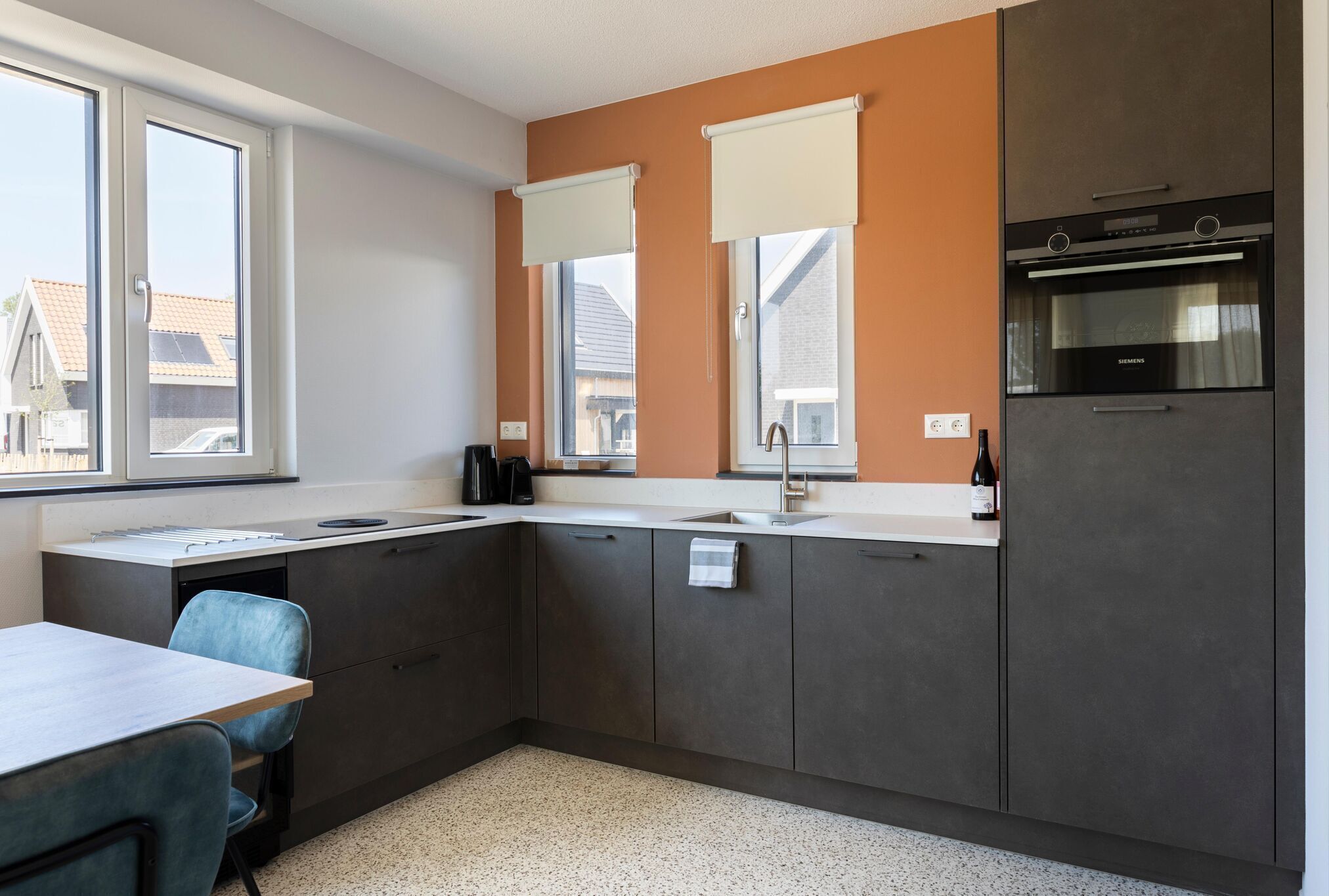 A modern kitchen with dark cabinets, a built-in oven, and a window with blinds.