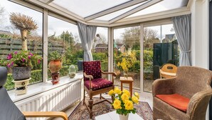 Ein Wintergarten mit Glasdach, einem Holzstuhl, einem rot gepolsterten Sessel und Topfpflanzen.