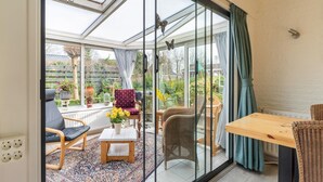 Ein Wintergarten mit Glastür, Korbmöbeln und einem Tisch mit Blumen.