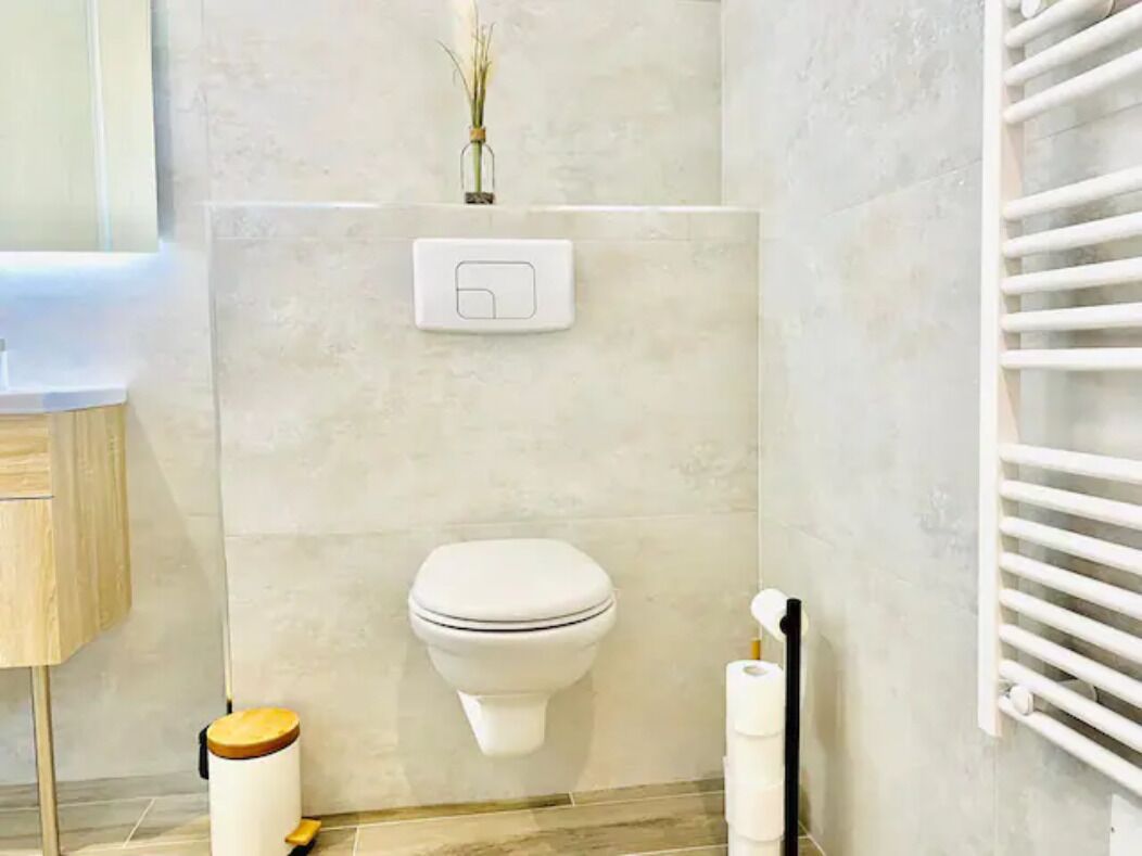 A modern bathroom with a toilet, a hand dryer, and a toilet paper holder.