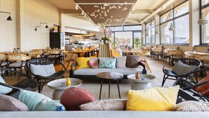 Un café spacieux doté de plusieurs espaces de détente, notamment des canapés et des fauteuils, ainsi que d’un espace de restauration central avec des tables et des chaises.