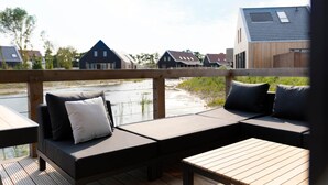 Une terrasse en bois avec un canapé et une table, donnant sur une rivière, avec des maisons en arrière-plan.