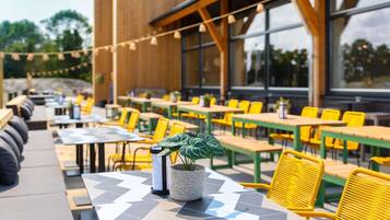 Un espace de restauration en plein air avec des chaises et des tables jaunes, une plante en pot et un présentoir à menus.