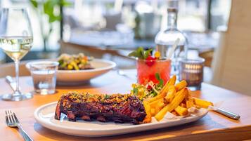 A plate of steak with fries and a salad, a glass of white wine, and a cocktail on a wooden table.
