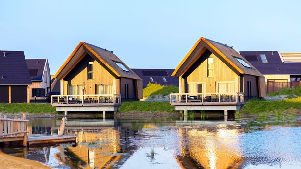 Two modern wooden houses with balconies over a calm water body, connected by a wooden bridge. - Holiday Home near North Sea Beach with Sauna (Nieuwvliet)