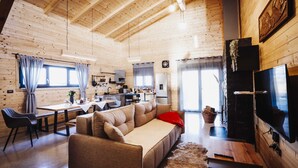 A cozy wooden cabin interior with a sofa, dining table, kitchen area, and a television.
