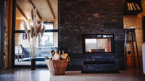 A cozy living room with a stone fireplace, a wicker basket with firewood, and pampas grass.