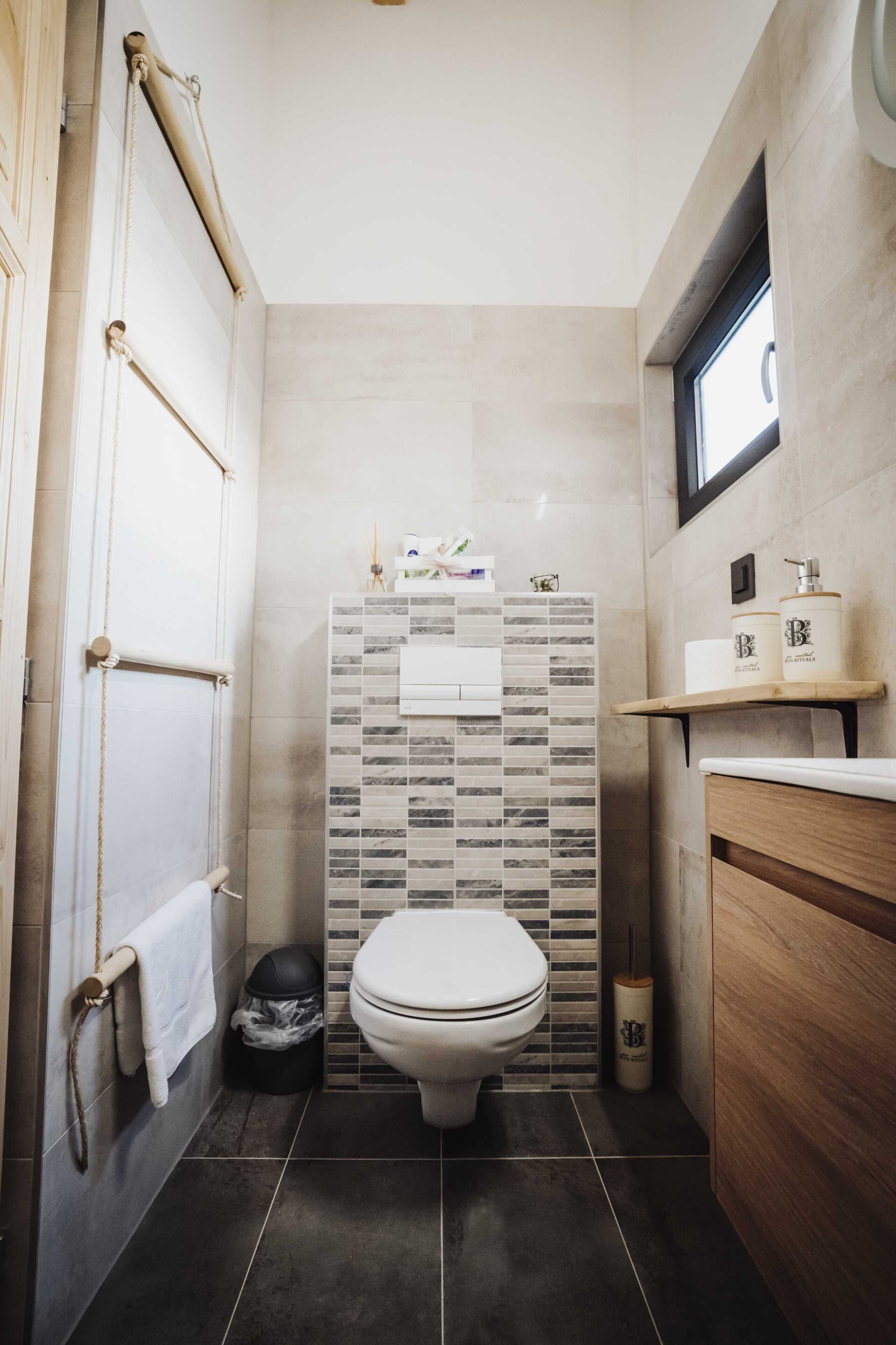 A compact bathroom with a toilet, a shower area, a small shelf with toiletries, and a wooden cabinet.