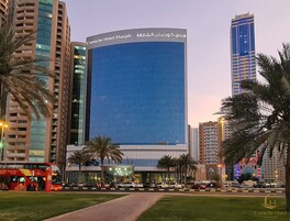 Un edificio de hotel con un letrero llamativo, rodeado de palmeras y otros edificios altos.