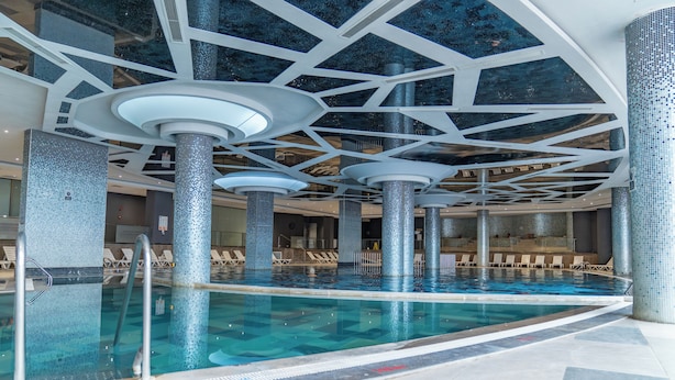 Piscina com design geométrico no teto, cadeiras de descanso e piso em azulejo.