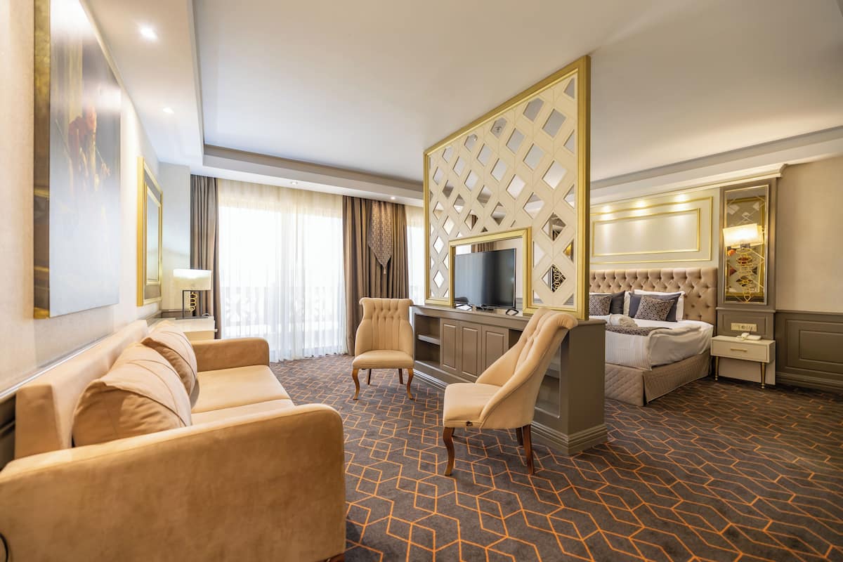 Una habitación de hotel con sofá, sillones, cama, televisor y escritorio.