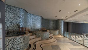 Um interior moderno com área de estar curva, paredes revestidas em azulejos e guarda-corpo de vidro com vista para uma piscina.