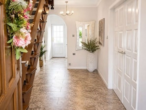 A hallway with a wooden staircase, a white door, a large mirror, and a potted plant.