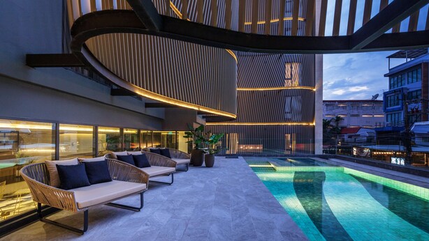 Un espace de détente extérieur moderne, doté d’une piscine, de sièges et offrant une vue sur le paysage urbain.