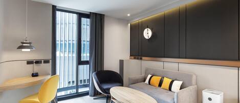 Una habitación de hotel moderna con sofá, una silla, una mesita, un calentador portátil y una ventana con cortinas.