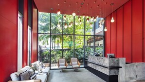 Un espace d’accueil moderne avec un mur rouge, un comptoir d’accueil en marbre et deux fauteuils blancs.