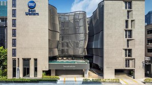Un hôtel Best Western moderne, doté d’une façade originale ornée de motifs à rayures de zèbre, d’un espace piscine et d’un ciel dégagé en arrière-plan.