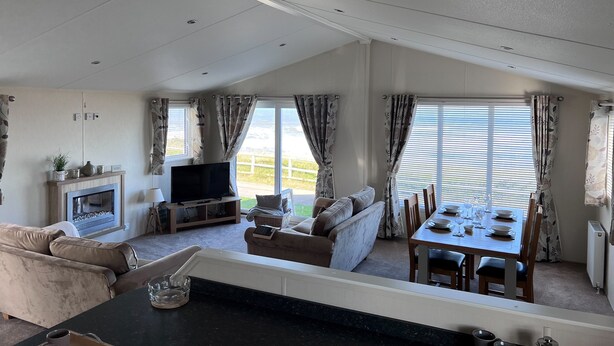 A spacious living area with a sofa, TV, fireplace, dining table, and large windows. - Beautiful Lodge w/Amazing Coastal Views (Hartlepool)