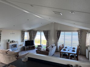 A spacious living area with a sofa, TV, fireplace, dining table, and large windows. - Beautiful Lodge w/Amazing Coastal Views (Hartlepool)